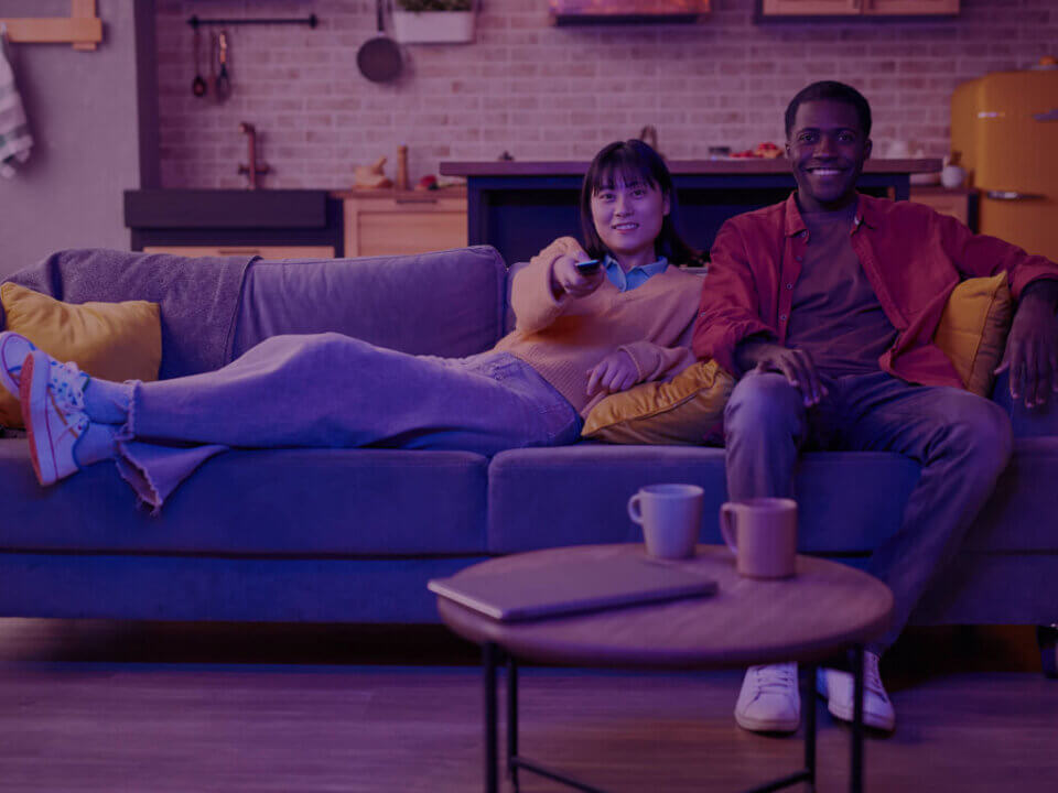 A young couple relaxing on a couch, watching TV.