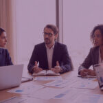 Senior Amazon team in a modern meeting room reviewing marketplace performance together on laptops.