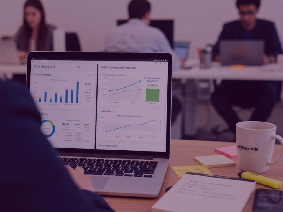 Amazon Ads incrementality dashboard in strategy meeting - Venture Forge Advertising Manager reviewing an Amazon Ads incrementality dashboard on a laptop during a strategy meeting, showing AMC analytics