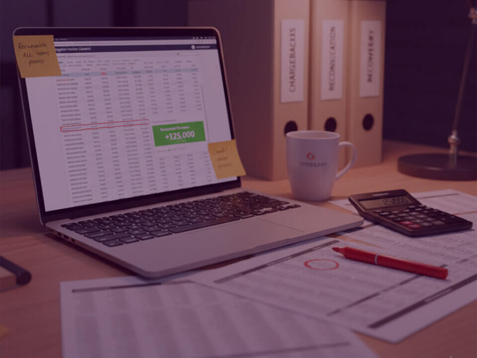 Amazon chargeback recovery audit workspace - Venture Forge Laptop showing an Amazon chargeback reconciliation spreadsheet highlighting £125,000 recovered, with calculator, paperwork and chargeback folders on a desk.